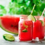 Fresh red watermelon slice and smoothie in glass jar with straw, ice, mint, lime on light background, copy space